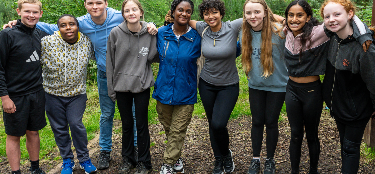 young people in a line smiling to camera in the forest